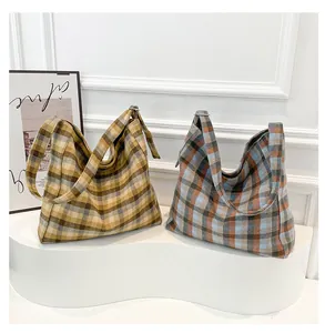 Detail view of two plaid canvas tote bags in warm and cool tones on white display stands