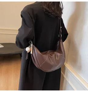 Detail view of brown leather croissant bag with white stitching and baseball charm