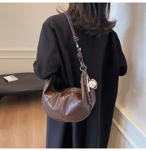 Close-up of brown pleated crescent shoulder bag with a creative baseball charm accessory