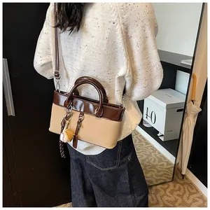 Detail of two-tone tote bag in beige and coffee with baseball pendant accessory