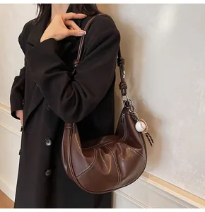 Detail view of brown hobo bag with contrast stitching and baseball charm on shoulder strap