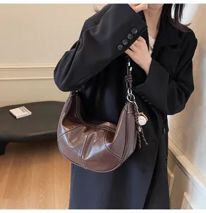 Close-up of brown hobo bag with contrast stitching and baseball charm on a shoulder strap