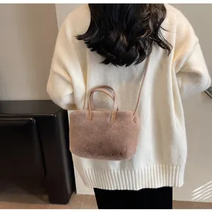 Détail d'un sac à main en peluche rose poudré porté avec un gros pull en maille blanc