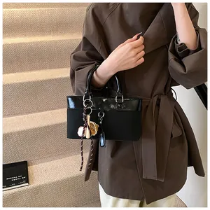 Detail of black tote with mixed leather textures and baseball charms held by model