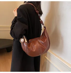 Detail of dark brown hobo bag featuring contrast white stitching and baseball charm
