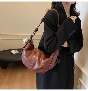 Brown leather crescent bag detail featuring knotted strap and baseball charm on shoulder