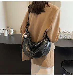 Detail of black hobo bag with white stitching and baseball charm on a coffee shop background
