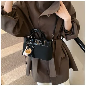 Detail of black tote bag with mixed patent leather finish and baseball bag charm