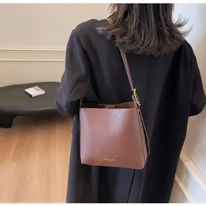 Detail of dark brown leather bucket bag with gold fashion text and wide strap on model