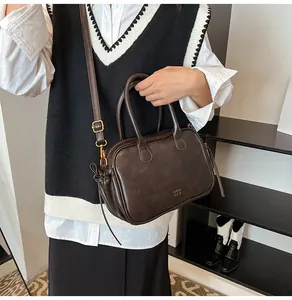 Detail of a dark brown matte leather crossbody bag with dual handles and brand logo