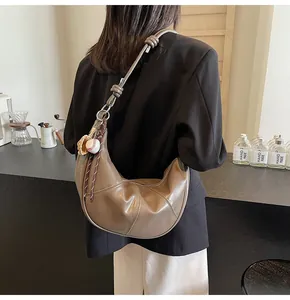 Detailed shot of brown crescent shoulder bag with baseball charms and stitching detail