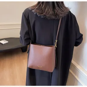 Close-up of brown leather bucket bag with gold fashion text and metallic hardware details