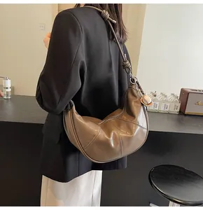 Detail of a brown leather crescent bag with baseball charm on a model's shoulder