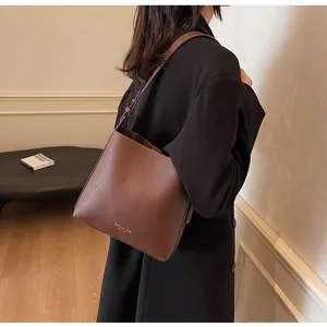 Brown leather bucket bag with wide strap worn by a model in a minimalist room
