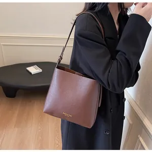 Detail of dark brown leather bucket bag with gold lettering on adjustable shoulder strap