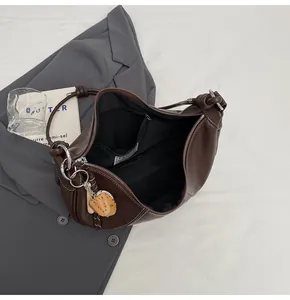 Detail of dark brown leather crescent bag with inner pocket and baseball glove charm