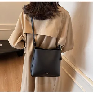 Detail of a black leather bucket bag with gold lettering styled on a beige trench coat