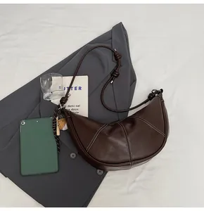 Detail of dark brown croissant bag with white stitching and baseball glove charm