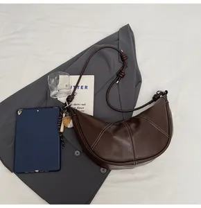 Detail view of brown croissant bag with white contrast stitching and knotted shoulder strap