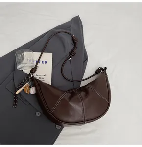 Close-up of brown crescent bag featuring white contrast stitching and a baseball charm