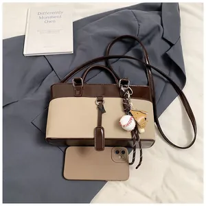 Brown and beige tote bag with a sports charm next to a phone for size comparison