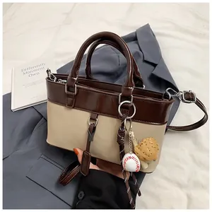 Detail of two-tone tote bag with baseball pendant and shoulder strap on a blue blazer