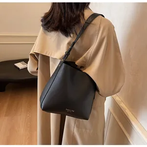 Detail of a black leather bucket bag with gold lettering shown on a model's shoulder