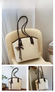 Close-up of off-white tote bag with dark brown straps and metal logo detail