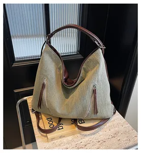 Detail of high-capacity grey canvas hobo bag with brown leather trim and metal zippers