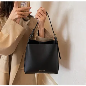 Detail of black bucket bag showing gold logo and adjustable shoulder strap with buckle