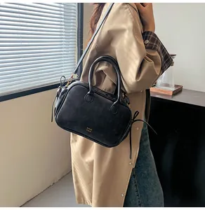 Style detail of a black matte leather crossbody bag worn over a beige trench coat