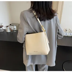 Detail of cream leather bucket bag with wide strap and gold hardware on model