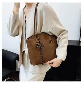 Detail of vintage brown tote bag with woven pendant and shoulder straps in neutral room