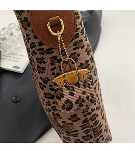 Detail of leopard print tote featuring brown leather tabs, gold D-rings, and mini bag charm