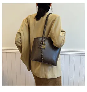 Detail of dark brown tote bag featuring embossed text and a metal tennis racket charm