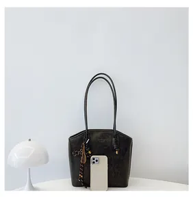 Detail of dark gray tote bag with textured finish, shoulder straps and decorative charm