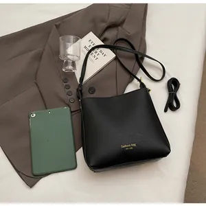 Flat lay of black leather bucket bag with wide shoulder strap on a bed setting