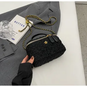 Detail of black tweed crossbody bag with gold flower hardware and chain strap on grey blazer