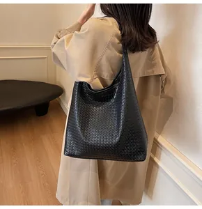 Gros plan sur la texture du sac cabas tissé noir porté par une femme en trench-coat beige