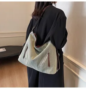 Detail of grey-green fabric tote with brown leather straps and front zippers worn by model