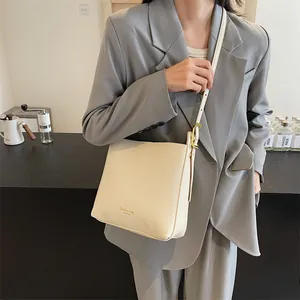Cream leather bucket bag with adjustable strap and golden hardware worn by a model