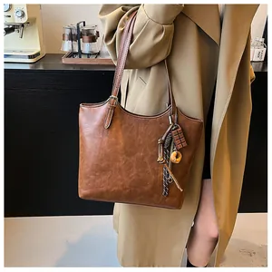 Grande borsa tote vintage marrone con ciondoli indossata da modella in trench beige