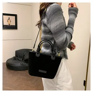 Detail of black suede-textured bucket bag featuring knotted handle and brand logo