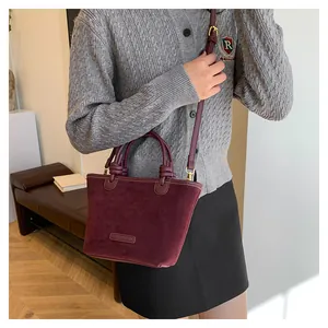 Detail of burgundy suede tote bag with gold metal buckles and adjustable shoulder strap