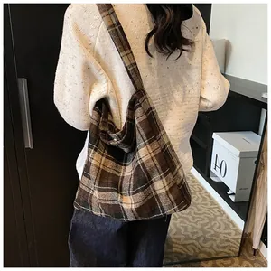 Detail van een grote bruine geruite hobo-tas gedragen door een model in een witte trui