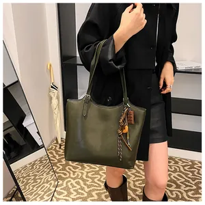 Dettaglio della borsa tote verde scuro con ciondoli decorativi sulla tracolla in città