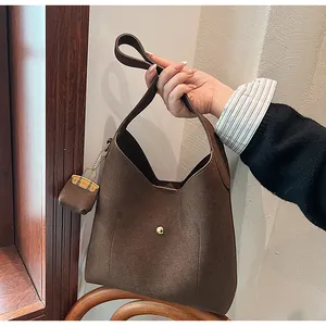 Macro view of dark brown suede hobo bag with gold buckle and mini charm detail