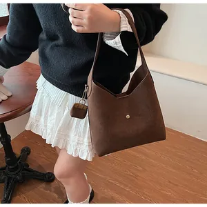 Detail of dark brown suede shoulder bag with magnetic gold clasp and mini charm accessory