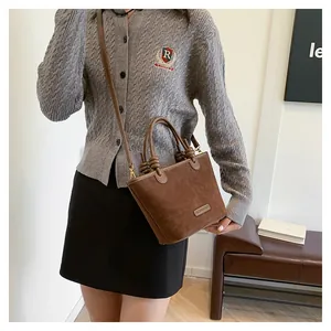 Detail of dark brown suede bucket bag featuring knotted handle and metallic logo plaque