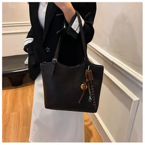 Dettaglio borsa tote in pelle marrone scuro con tracolla regolabile e ciondolo in metallo